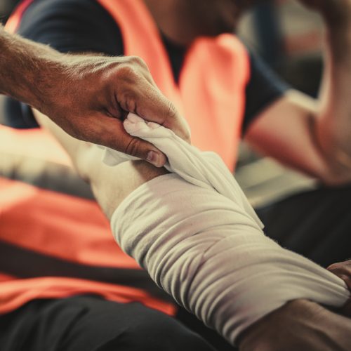 Taking care of physical injury at work! Close up of unrecognizable manual worker assisting his colleague with physical injury in a warehouse.